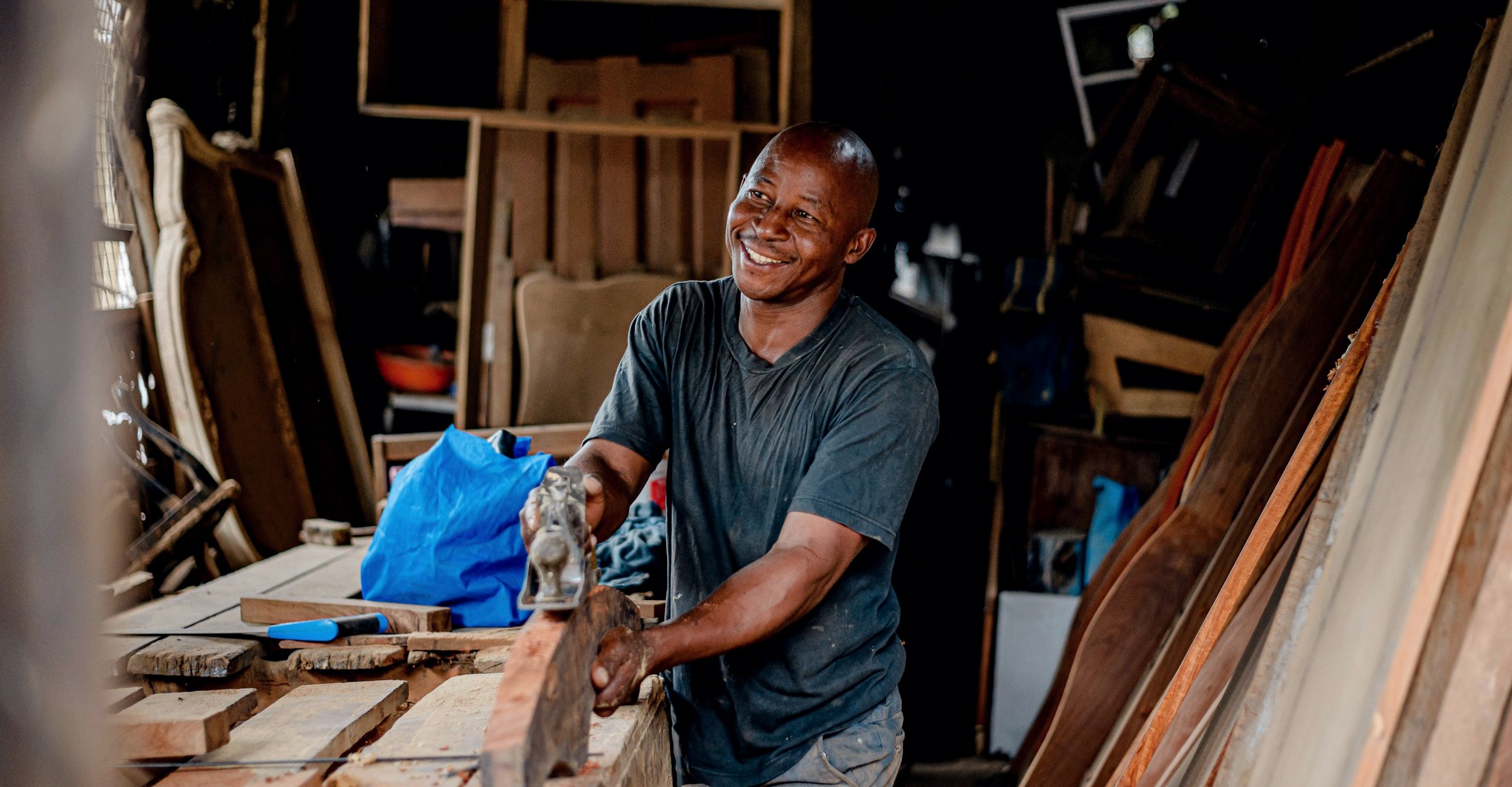 A smiling craftsman planing wood in his workshop