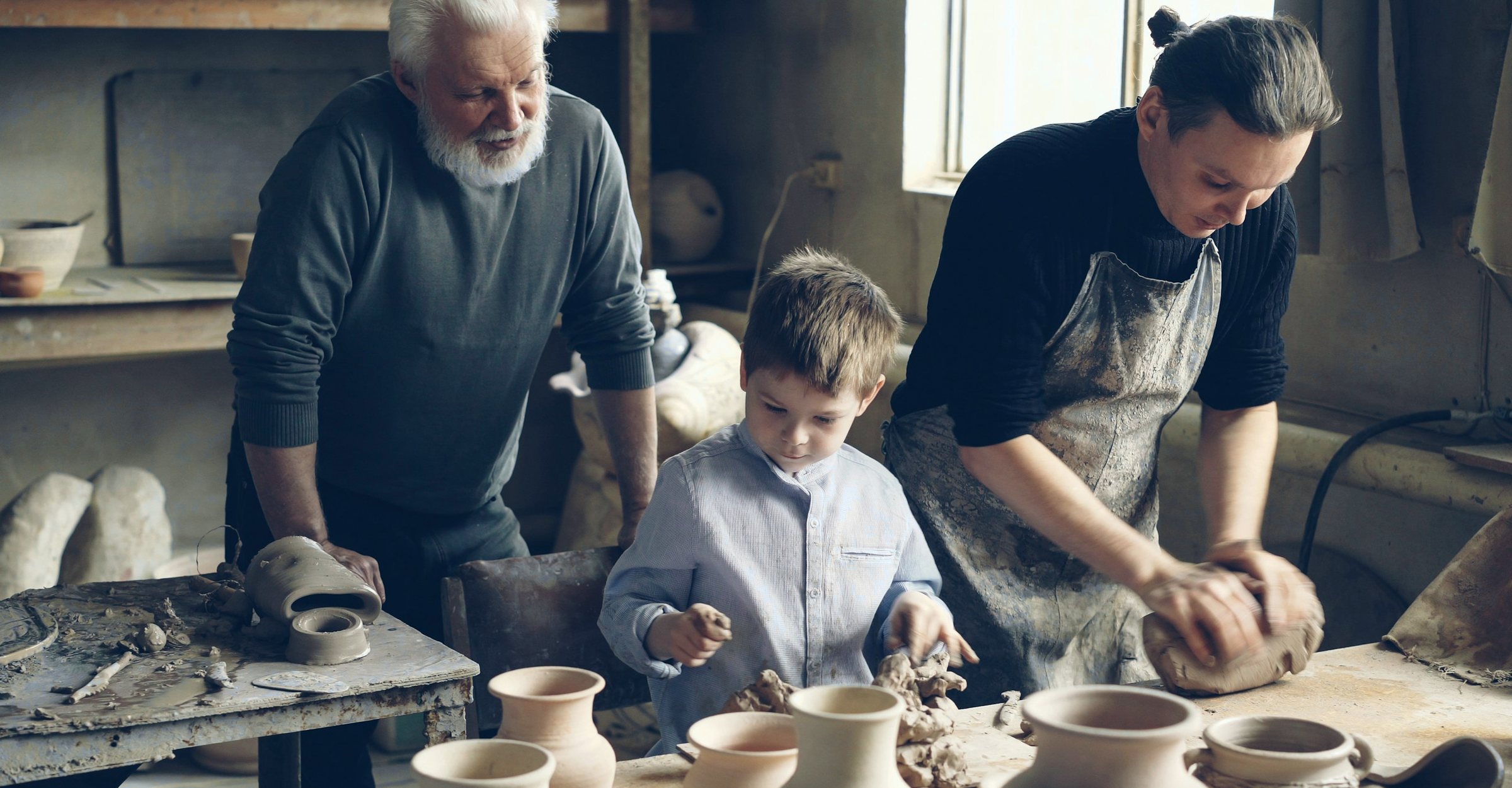 A grandfather, a parent and a child working together in a pottery workshop